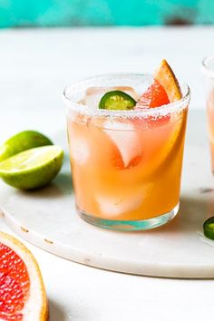 two glasses filled with drinks sitting on top of a white plate next to limes and grapefruit