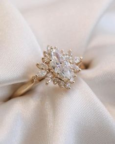 an engagement ring is sitting on top of a white satin material with diamonds in the center