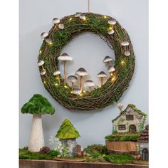 a wreath with mushrooms and fairy lights hanging on the wall next to a shelf filled with miniature houses