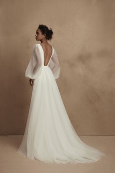 a woman in a white wedding dress with open back and sheer sleeves, looking off to the side