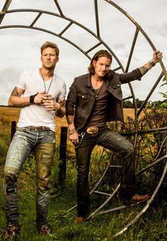 two men standing next to each other in front of a metal structure with plants growing out of it