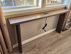 a long wooden table sitting in front of a window next to a wall with a phone plugged into it