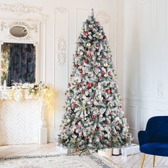 a white christmas tree with red and gold ornaments in a living room area next to a blue chair