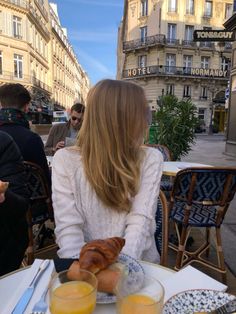 a woman sitting at a table with food and drinks in front of her on the street