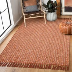 an orange rug with fringes on the floor in front of a chair and potted plant