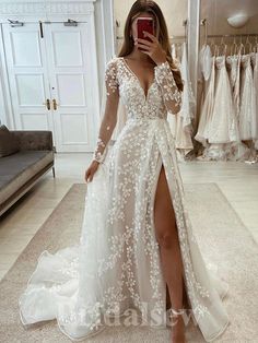 a woman taking a selfie while wearing a wedding dress with long sleeves and thigh high slit