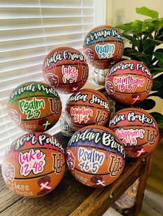 a pile of basketballs sitting on top of a wooden table next to a potted plant