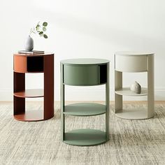 three different colored tables on carpeted floor next to white wall and potted plant