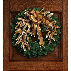 a christmas wreath with pine cones and gold bow hanging on a wooden frame in front of a door