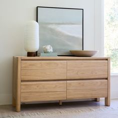 a wooden dresser with a bowl on top and a large mirror above it in a white room