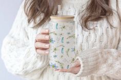 a woman holding a cup with a straw in her hand while wearing a white sweater