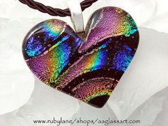 a heart shaped glass pendant on a black cord with a rainbow pattern in the middle