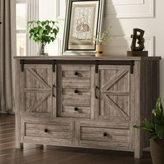 a large wooden cabinet with two doors and three drawers in front of a window next to a potted plant