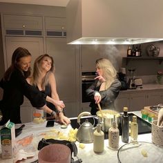 three women standing around a kitchen preparing food