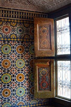 an ornately designed wall in a room with two windows and decorative tiles on the walls