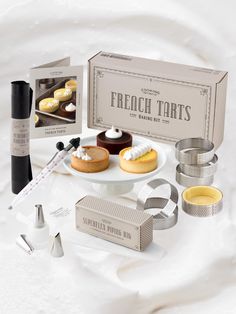 an assortment of french tarts on a white tablecloth with the box and tools used to make them