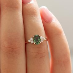 a close up of a person's hand holding a ring with a green stone