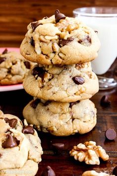 chocolate chip cookies stacked on top of each other next to a glass of milk and some chopped walnuts