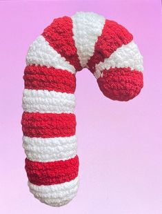 a red and white knitted candy cane on a pink background with the top off