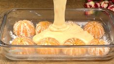 an orange being drizzled with icing in a glass dish on a wooden table