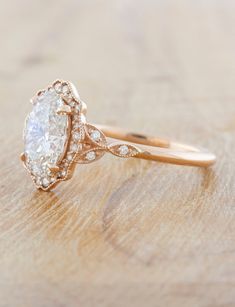 an oval shaped diamond engagement ring on top of a wooden surface with diamonds around the band