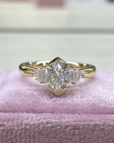 a three stone diamond ring sitting on top of a pink blanket