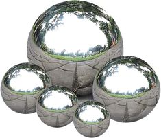 four silver balls sitting on top of each other with trees in the reflection behind them