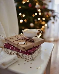 a stack of wrapped presents sitting on top of a white chair next to a christmas tree