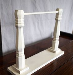 a white wooden stand with two posts on the top and one at the bottom, sitting on a wood table