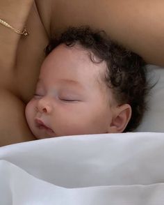 a close up of a baby laying in a bed with its head on someone's chest