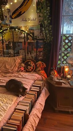 a cat laying on top of a bed covered in lots of books next to a window