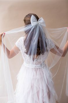 a woman in a white dress with a bow on her head and veil over her shoulder