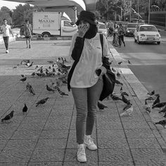 a woman walking down the street while talking on her cell phone and birds flying around