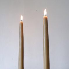 two lit candles sitting side by side in front of a white wall