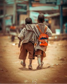 two young boys walking down a dirt road with backpacks on their back and one carrying a school bag