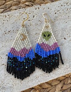 two pairs of beaded earrings sitting on top of a stone slab next to a wicker basket