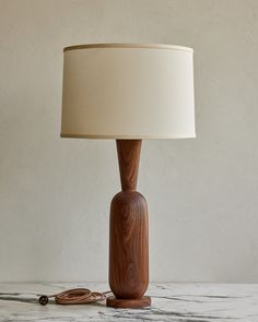 a wooden table lamp with a white shade on the base and a cord plugged into it