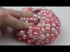 a hand holding a pink and white beaded object