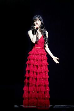 a woman in a red dress on stage with her hand up to her face and mouth