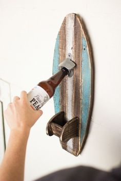 a person holding a beer bottle in front of a surfboard shaped like a hook