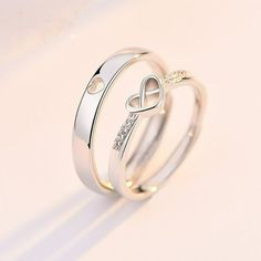 two white gold wedding rings with diamond accents on each side and an interlocked heart in the middle