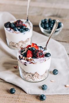 two small glass bowls filled with yogurt, berries and granola on top of a white cloth