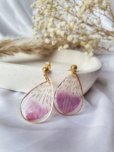 the pink and white flower earrings are sitting on top of a white plate next to dried flowers