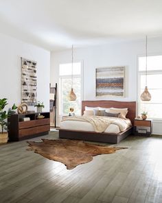 a bedroom with white walls and wood flooring has a large bed, two nightstands, an animal skin rug on the floor