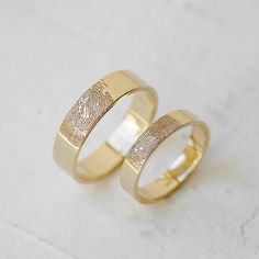 two gold wedding rings with fingerprints on the inside and outside, set against a white background