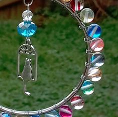 a bird is hanging from a circular metal object with colorful beads and charms on it