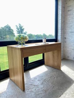 a wooden desk sitting in front of a window next to a vase with flowers on it