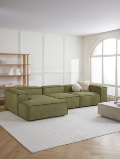 a large green couch sitting on top of a white rug in front of a window