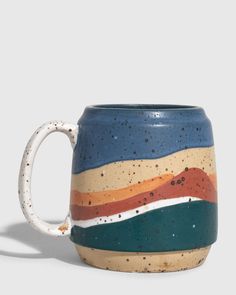 a ceramic mug with multicolored stripes on the outside and inside, sitting on a white surface