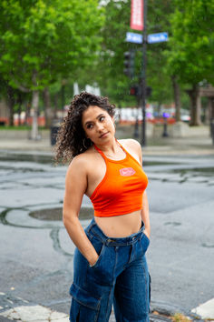 woman modeling upper park's club graphic baby rib halter top in orange in downtown chico, california standing on a street corner in the rain. modeling in the rain. rainy day photoshoot. Affordable Stretch Ribbed Halter Top, Ribbed Fitted Halter Neck Top, Summer Ribbed Crop Halter Top, Ribbed Fitted Halter Tank Top, Solid Ribbed Halter Tank Top, Ribbed Halter Top, Rain Or Shine, Halter Neckline, Halter Top